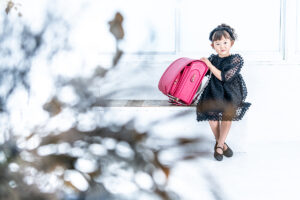小学校入学記念に7歳の女の子がランドセルと一緒にスタジオルーチェイリュームの撮影セットに笑顔で座っているシーン。