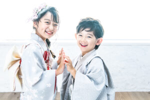 七五三記念に、7歳の女の子は振袖を5歳の男の子は羽織袴を着用し、スタジオルーチェイリュームで姉弟が手を繋ぎ笑顔を見せる様子。