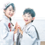 七五三記念に、7歳の女の子は振袖を5歳の男の子は羽織袴を着用し、スタジオルーチェイリュームで姉弟が手を繋ぎ笑顔を見せる様子。